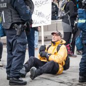 A older protester defiantly sits in fromt of Riot Police during Montreal's 18th annual Protest against Police Brutality.