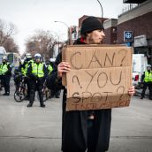 A protester holding a sign in front of Montreal Police.
